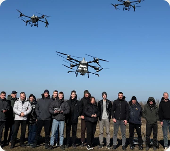 Група пілотів на полі з агродронами в небі